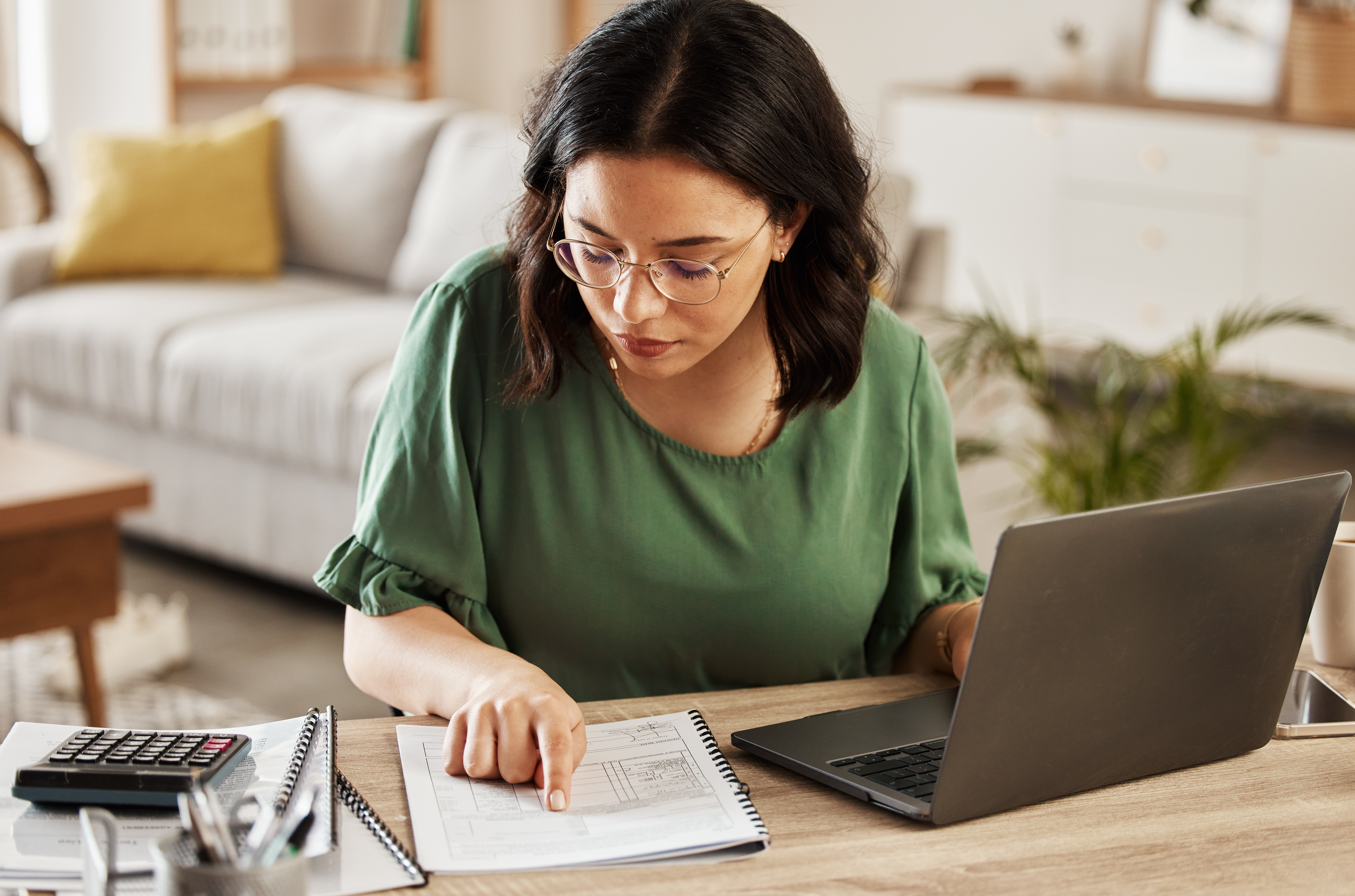 Middle aged senior woman sit with laptop and paper document. Pensive older mature lady reading paper bill pay online at home managing bank finances calculating taxes planning loan debt pension payment